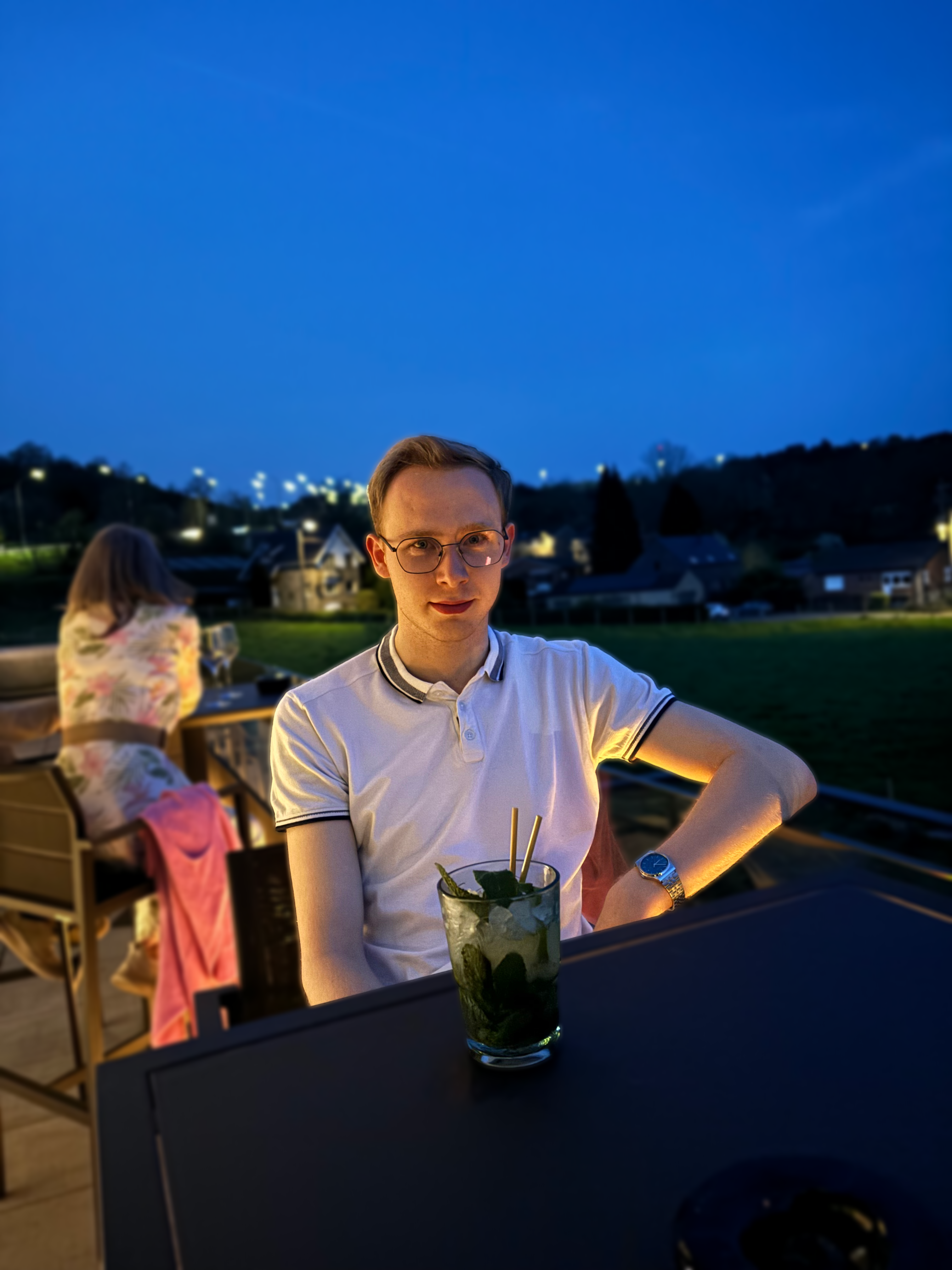 Person sitting at a table with a drink, with a scenic evening background